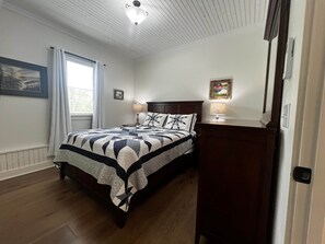 Une chambre à coucher avec un lit, deux lampes de chevet, une fenêtre avec des rideaux et une tête de lit en bois.