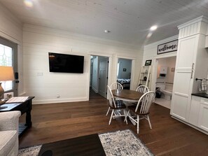 A dining area with a wooden table and chairs, a flat-screen TV mounted on the wall, and a 'welcome' sign above a doorway. - Charming Lodge 1.5 to Dollywood (Sevier County)