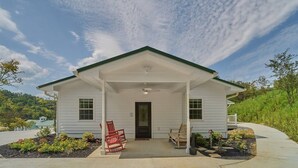 A single-story house with a covered porch, a front door, and a small garden area with flowers and a bench. - Charming Lodge 1.5 to Dollywood (Sevier County)
