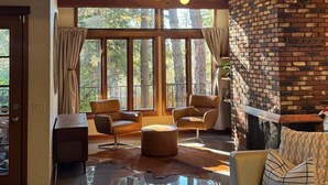 Un salón amplio con techo alto, ventanas grandes, sofás de cuero, una mesa de centro de vidrio y una chimenea de ladrillo.