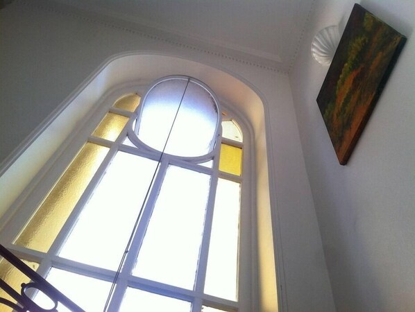 Una habitación con un gran ventanal de arco, un cuadro en la pared y una escalera.