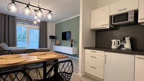 A modern kitchen with white cabinets, a microwave, and a coffee maker. There is a dining area with a wooden table and black chairs.