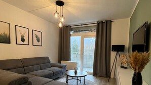 A modern living room with a grey sectional sofa, a round coffee table, and a flat-screen TV on a white cabinet.