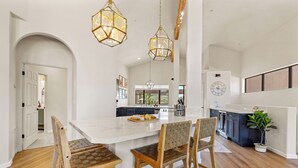 A spacious kitchen with a large island, wooden chairs, and pendant lighting.