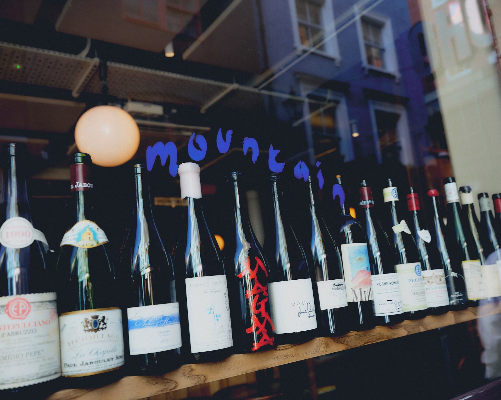 A row of wine bottles with labels, some with red ribbons, in a dimly lit setting.