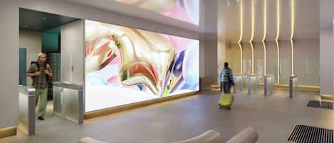 A modern lobby with a large digital art display, a seating area, and a check-in counter.