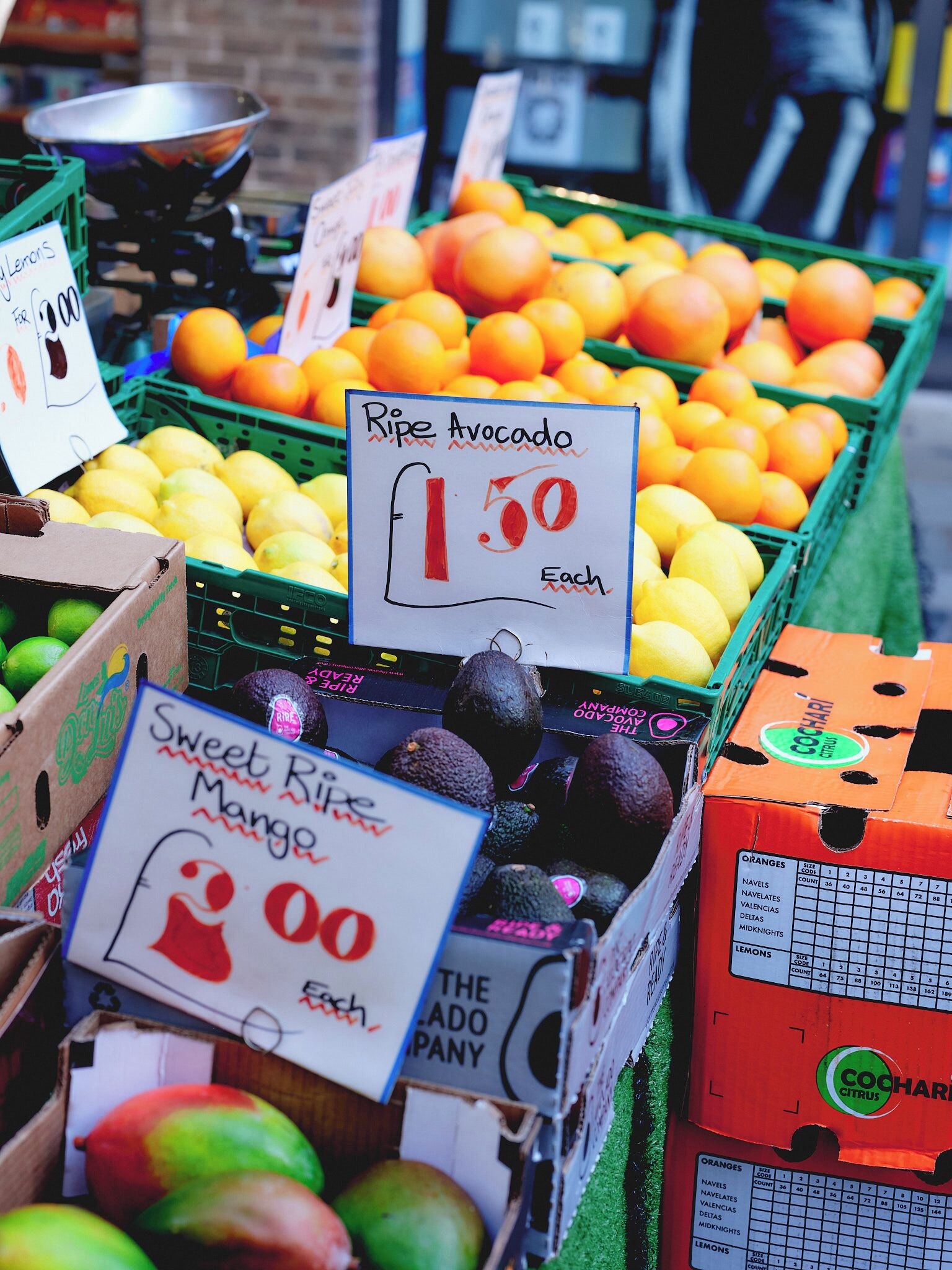 Un puesto de frutas con precios indicados para aguacates, limones y mangos.