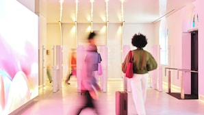 Un intérieur moderne avec un mur de verre, une personne avec une valise et un plafond éclairé en rose.