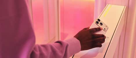 A person using a white device with a yellow stripe, possibly a control panel or kiosk, in a room with pink lighting.