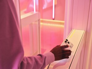 A person using a white device with a yellow stripe, possibly a control panel or kiosk, in a room with pink lighting. - Otherwander Soho Pod Hotel (ADULTS ONLY) (London)