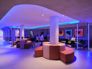 A modern lobby with seating areas, a large pillar, and a projection screen. - Otherwander Soho (London)