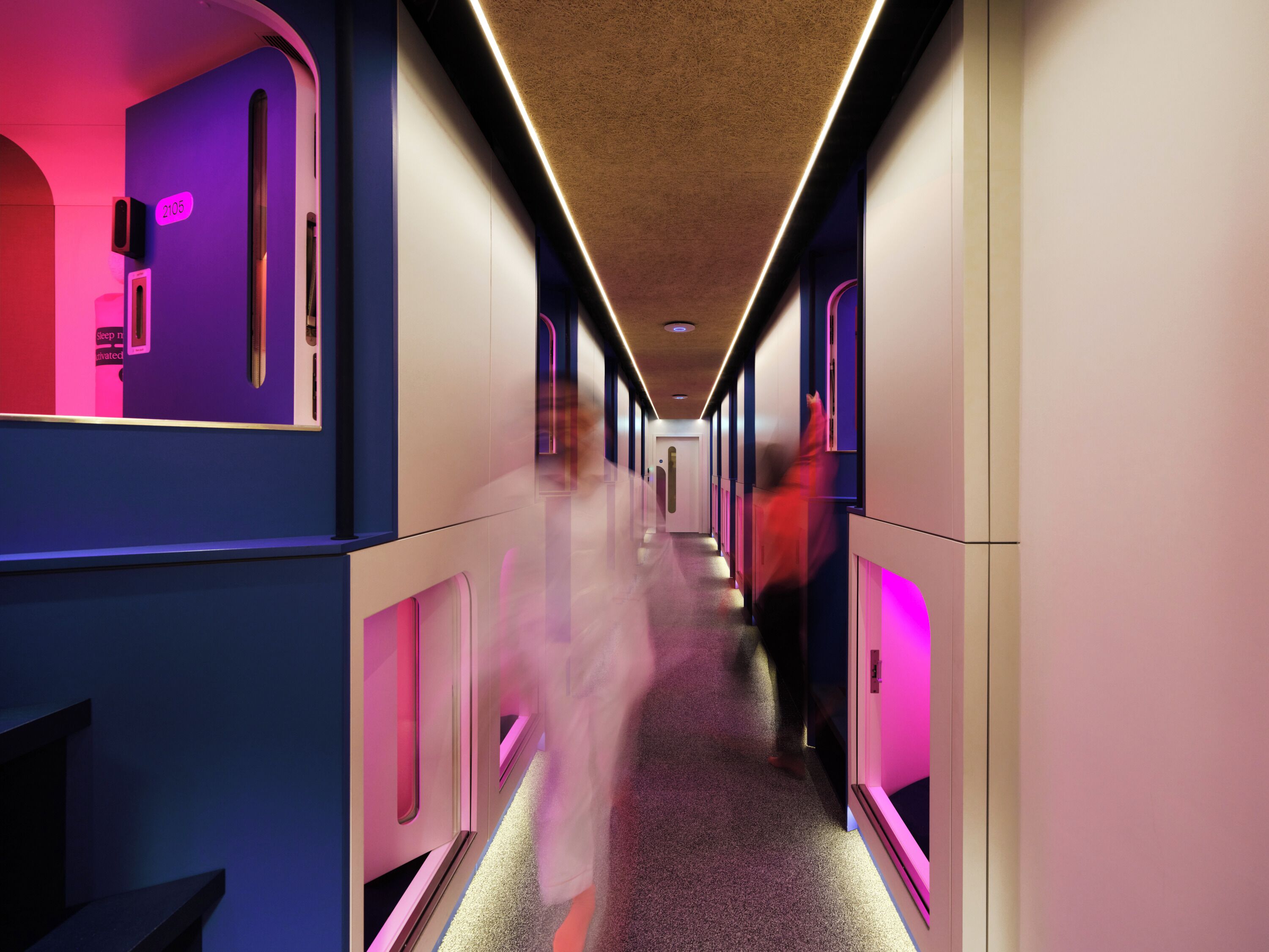 Un couloir de train moderne, avec un éclairage au plafond, une porte visible et une personne qui marche.