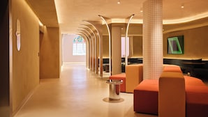 Un hall d’hôtel moderne avec un long couloir, des espaces de détente et une grande fenêtre ornée de vitraux.