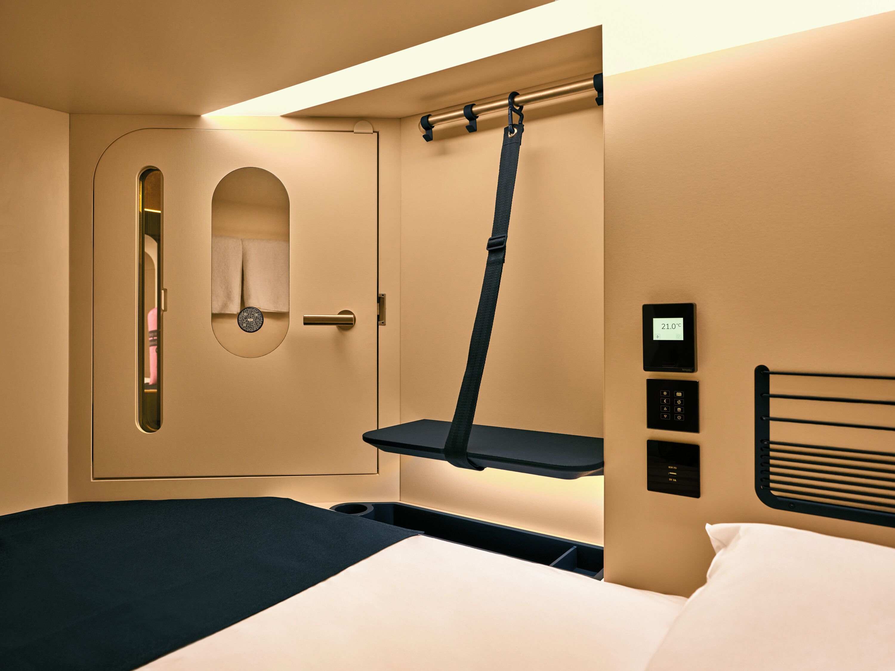 A hotel room with a bed, a bedside table, a control panel, and a door with a mirror.