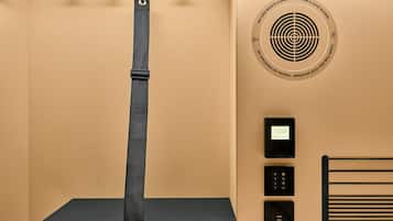 A room with a bed, a black shelf, a wall-mounted heater, and a smoke detector.