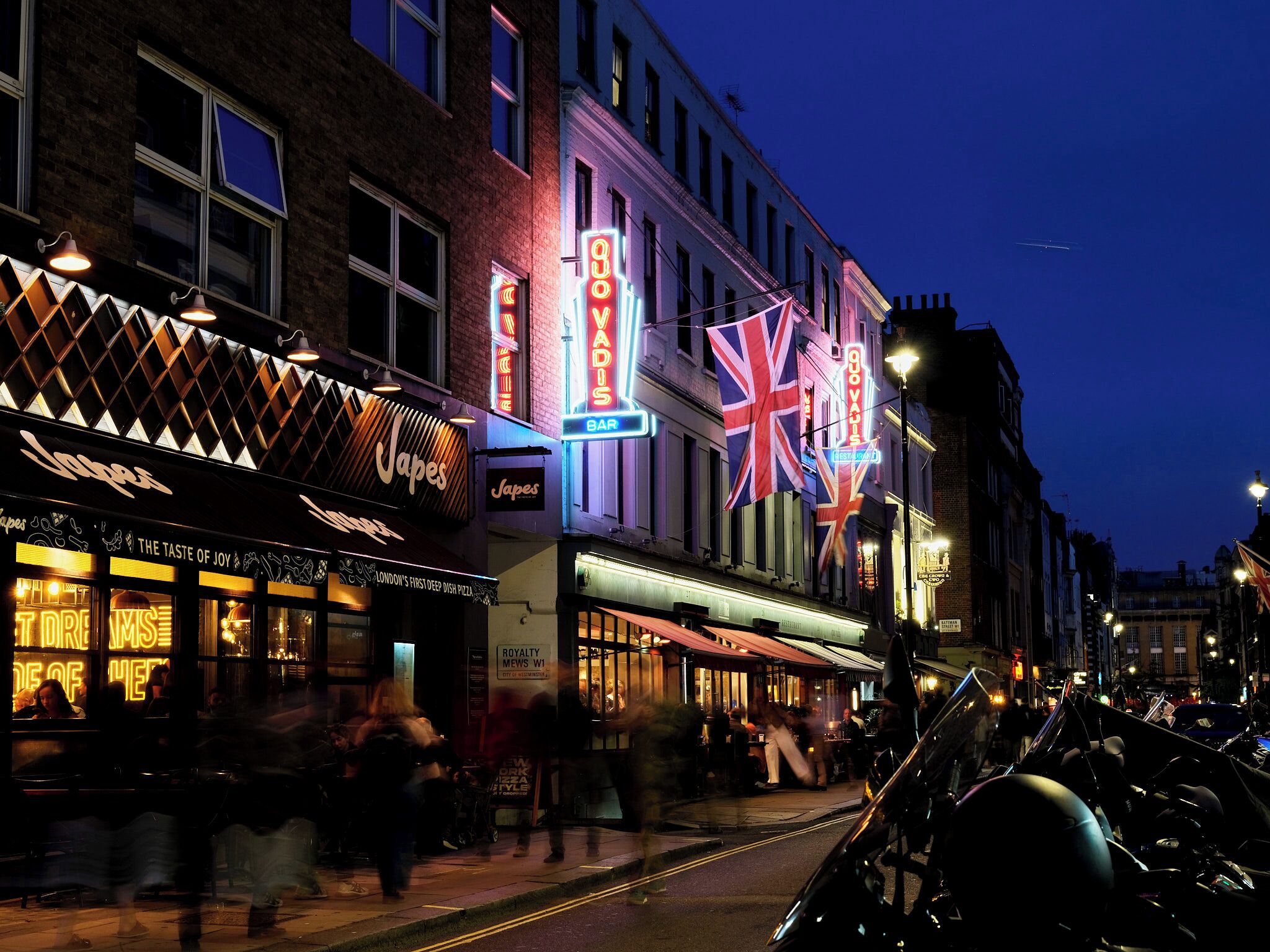 A street scene with illuminated storefronts, including a restaurant named 'Japes' and a bar.