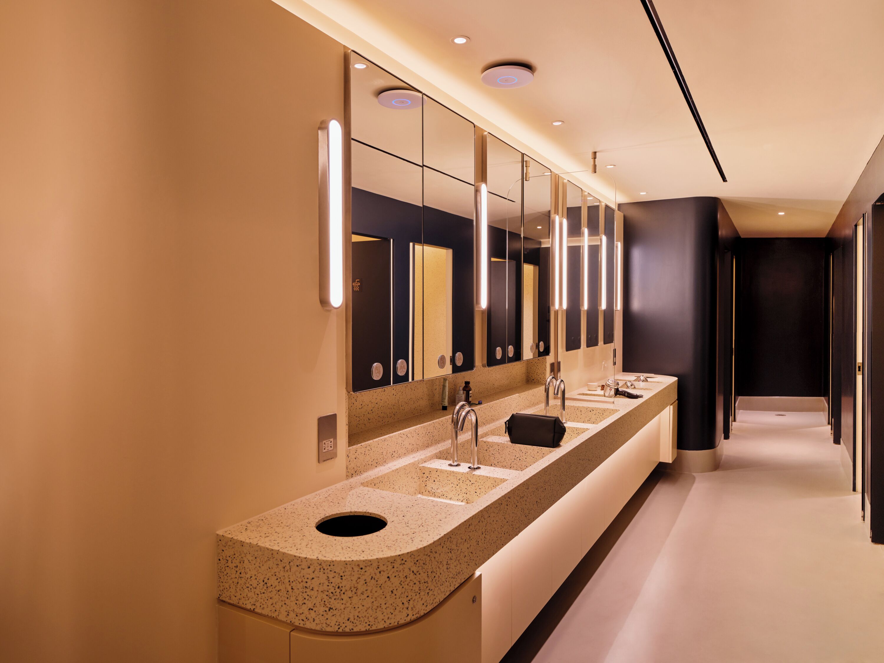 Un baño moderno con un tocador largo, varios espejos y una pared oscura.