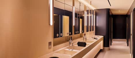Un baño moderno con un tocador largo, varios espejos y una pared oscura.