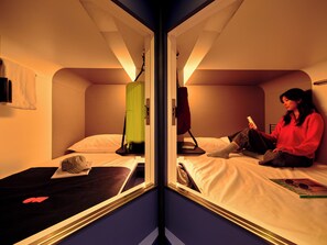 A mirrored room with a bed, a chair, and a person reading a book. - Otherwander Soho Pod Hotel (ADULTS ONLY) (London)