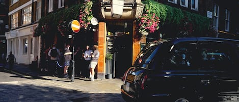 A street scene with a building featuring a brick facade, a sign reading 'BROADWICK STREET,' and a black car parked on the street.