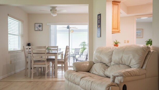 Ein Wohnzimmer mit einem beigefarbenen Sofa, einem Esstisch mit Stühlen, einem Deckenventilator und Blick durch eine Glastür.