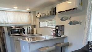 A compact kitchen with a central island, two bar stools, a microwave, a sink, and a coffee maker.