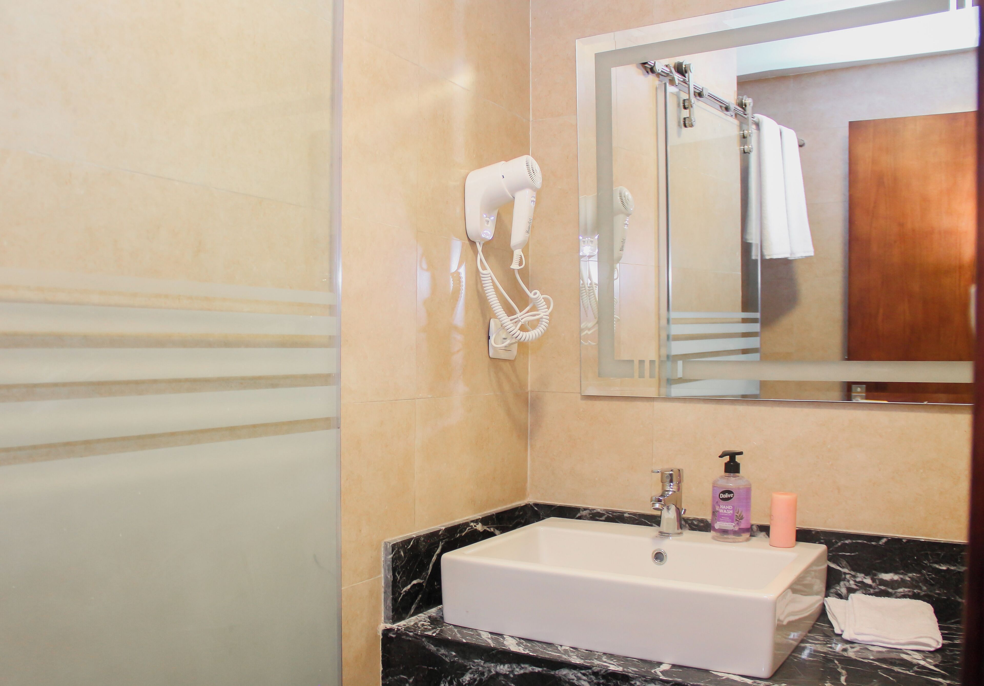 Un bany amb un lavabo de marbre, un assecador de cabells petit, un mirall i una zona de dutxa.