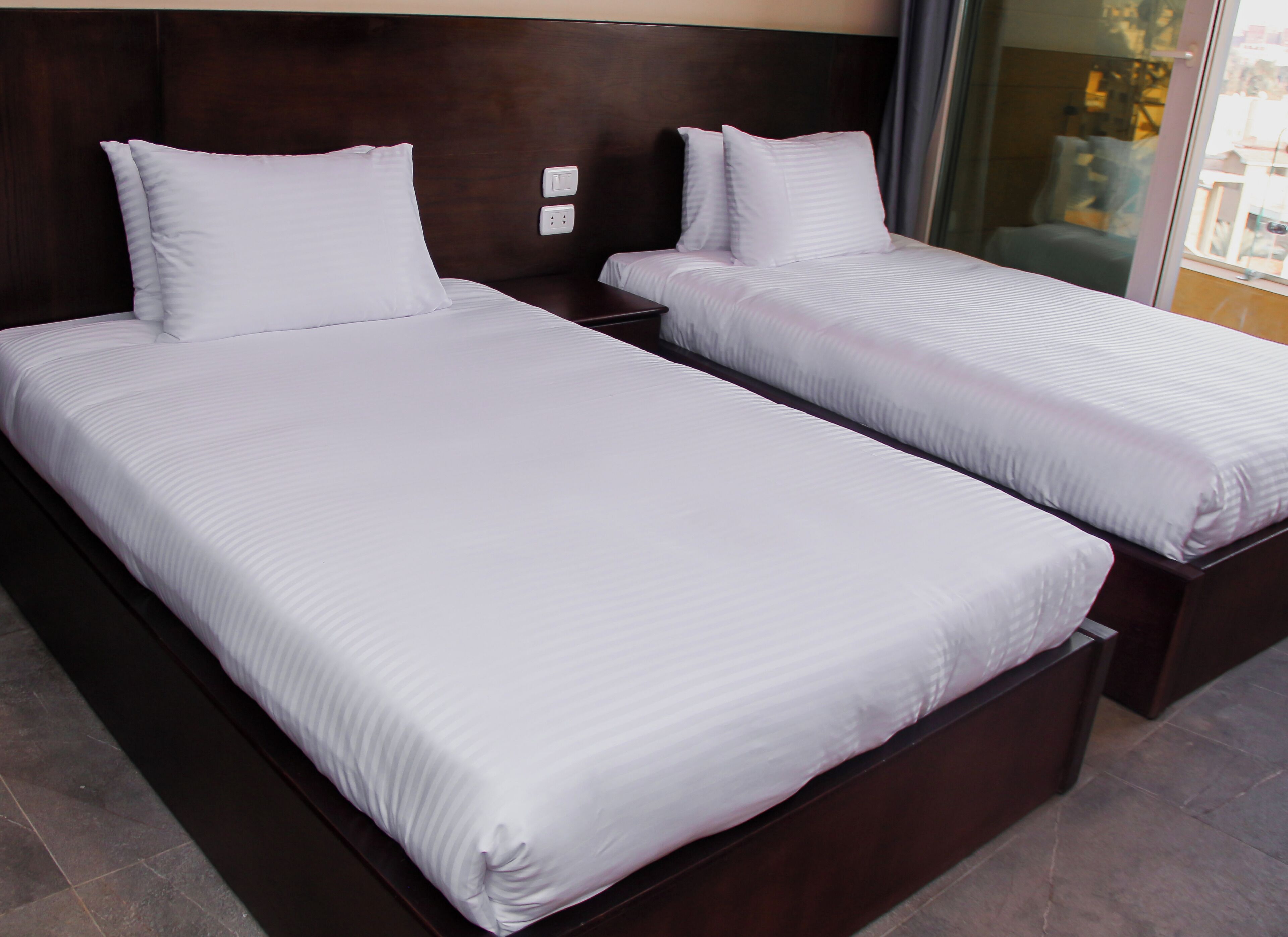 A hotel room with two single beds, dark wood headboards, white linens, and a modern design.