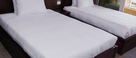 A hotel room with two single beds, dark wood headboards, white linens, and a modern design.