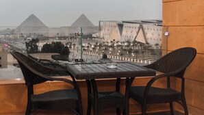 Un balcón con sillas de mimbre y una mesa, con vistas a pirámides y edificios modernos.