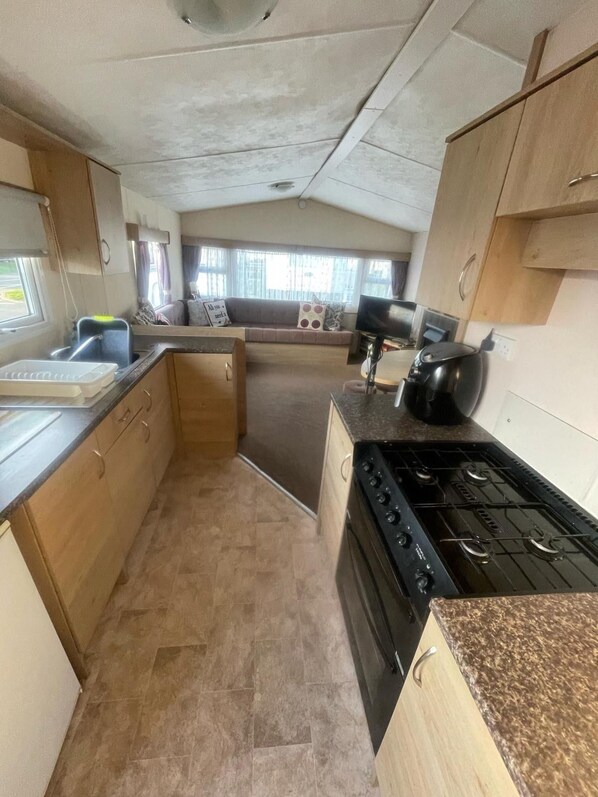A compact kitchen with a stove, sink, and cabinets. - 3 Bed Caravan - Sleeps 8 - Pets - Parking - Wifi (Rhyl)