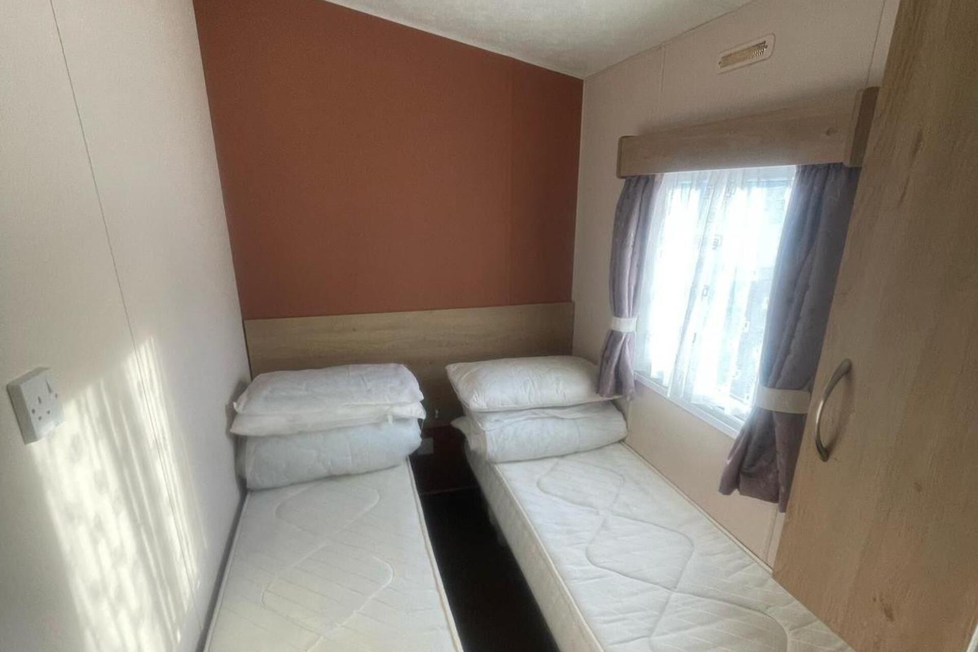 A small, single-room RV with two beds and a window with curtains.