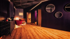 Un intérieur moderne avec un plancher en bois, un fauteuil rouge, un canapé et un coin bar équipé de verres et d’une machine à café.