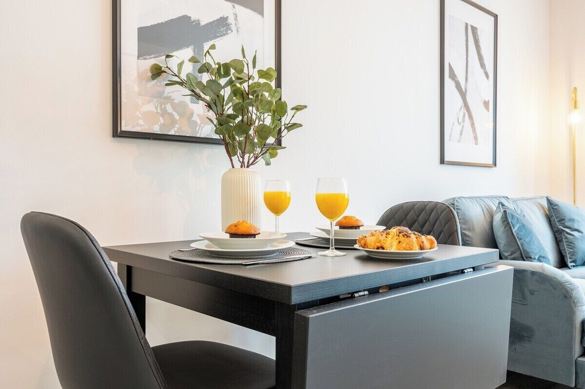 A modern dining area with a table set for breakfast, including muffins and orange juice, and a plant in a white vase.