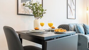 Un'area pranzo moderna con tavolo apparecchiato per la colazione, inclusi muffin e succo d'arancia, e una pianta in un vaso bianco.