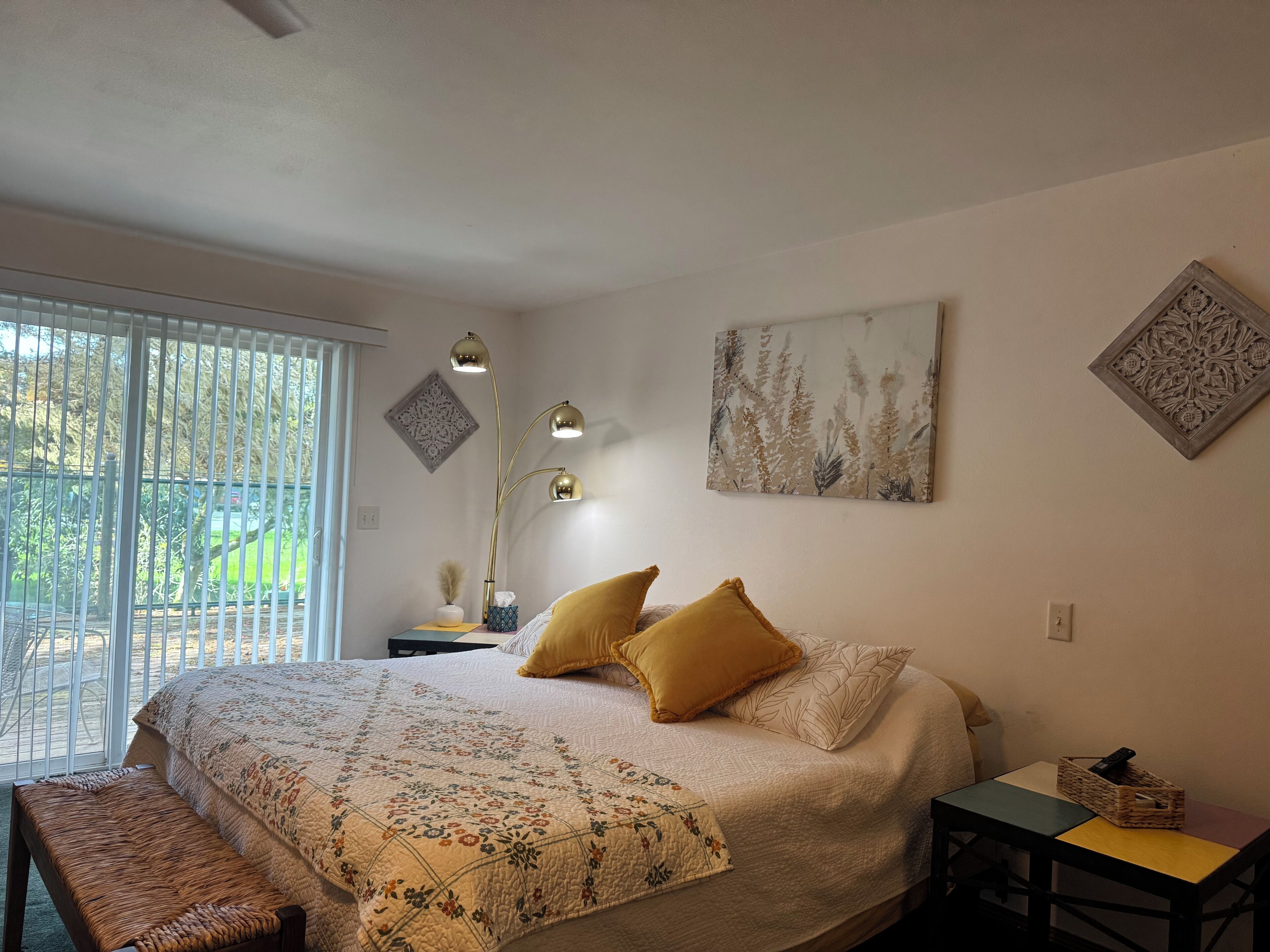 A bedroom with a large bed, a bench, a table, and a window with blinds.