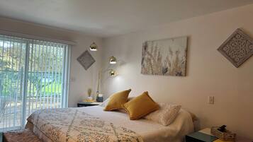 A bedroom with a large bed, a bench, a table, and a window with blinds.