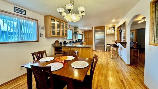 A dining area with a wooden table and chairs, a chandelier, and a view of the kitchen and living area.