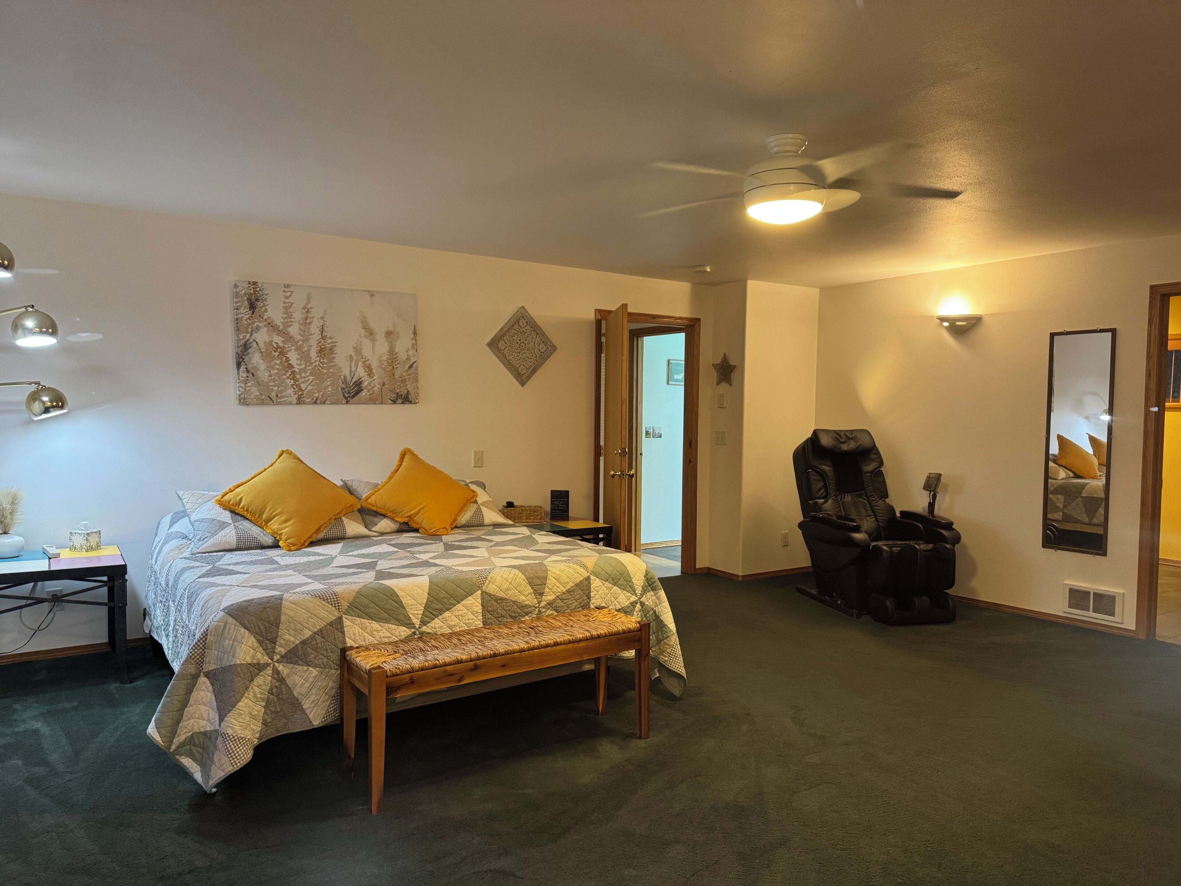 Un dormitorio con una cama, un banco, una silla, un ventilador de techo y una puerta.