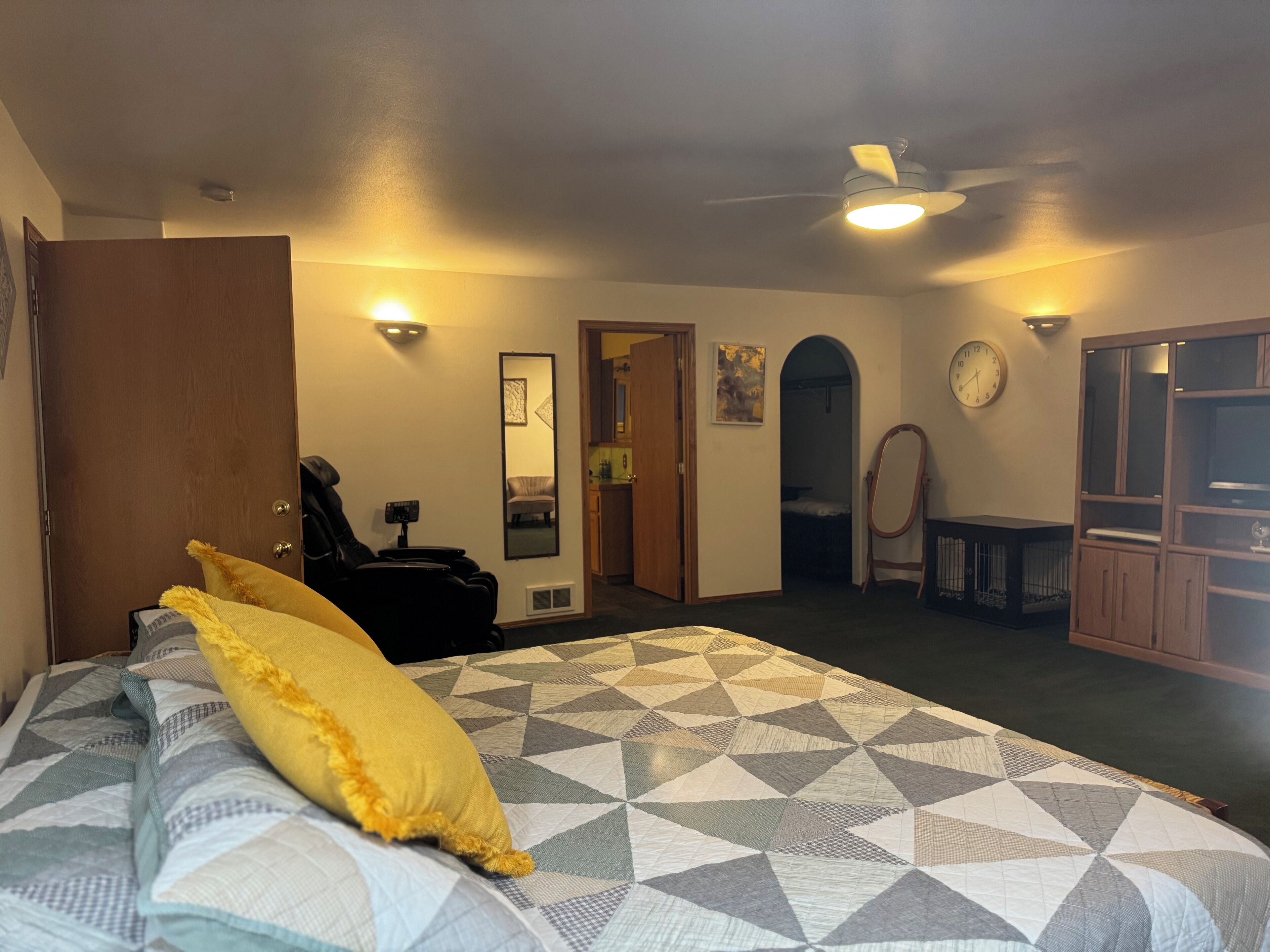 Een slaapkamer met een bed, een plafondventilator, een deur, een spiegel en een klok aan de muur.