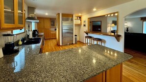 A kitchen with granite countertops, stainless steel appliances, wooden cabinets, and a bar area with stools.