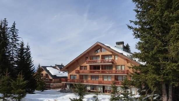 Een meerlaags hotel met balkons en een skipiste op de achtergrond.