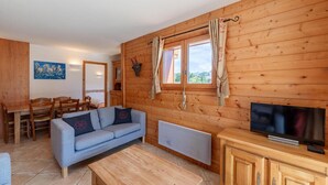 Un'accogliente stanza con pareti in legno, un divano, una TV e un'area pranzo con sedie e un tavolo.