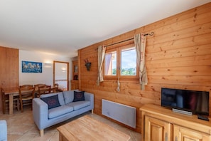 A cozy room with wooden walls, a sofa, a TV, and a dining area with chairs and a table.