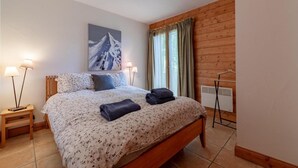 Una camera da letto con un letto in legno, due lampade ai comodini, un quadro raffigurante una montagna, un termosifone e una finestra con tende.