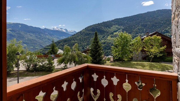 Un balcone con vista su un paesaggio montuoso, una recinzione in legno e un muro di pietra.