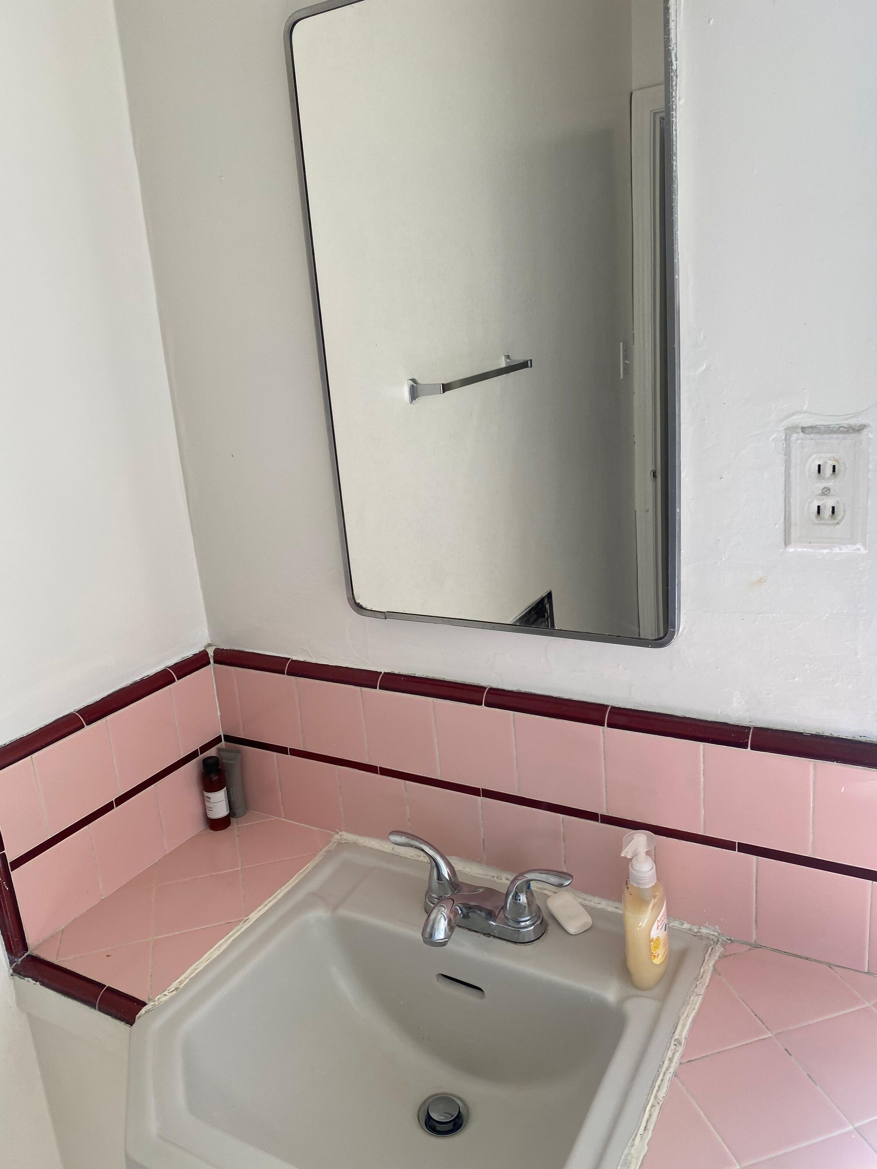 Un baño con lavamanos, espejo y paredes cubiertas de azulejos rosas.
