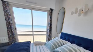 Een hotelkamer met een bed, een raam met uitzicht op het strand, een spiegel en een wandlamp.