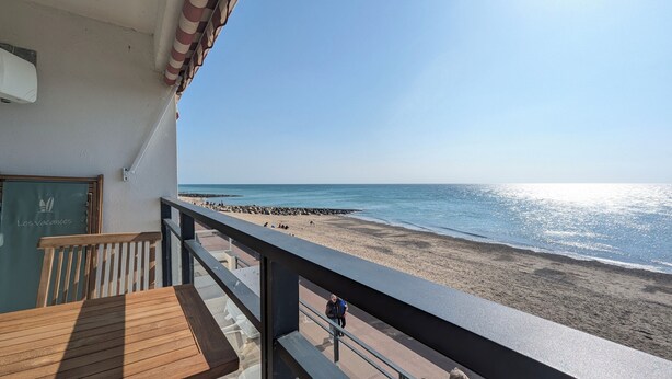 Een balkon met een houten tafel en uitzicht op een strand met een rotsachtige kustlijn.
