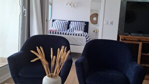 Een moderne hotelkamer met een groot bed, een televisie en twee donkerblauwe fauteuils.